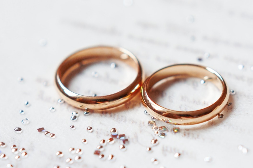 Golden wedding rings on paper invitation with shiny rhinestones. Wedding details, symbol of love and marriage.