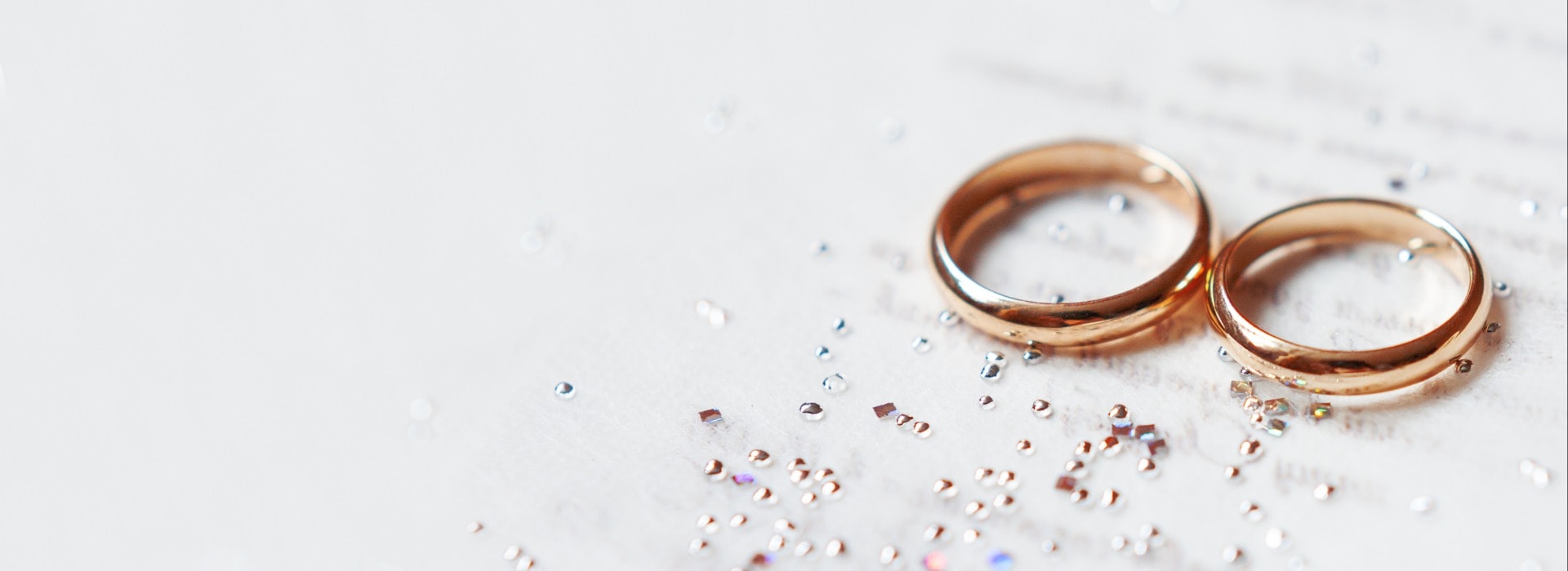 Golden wedding rings on paper invitation with shiny rhinestones. Wedding details, symbol of love and marriage.