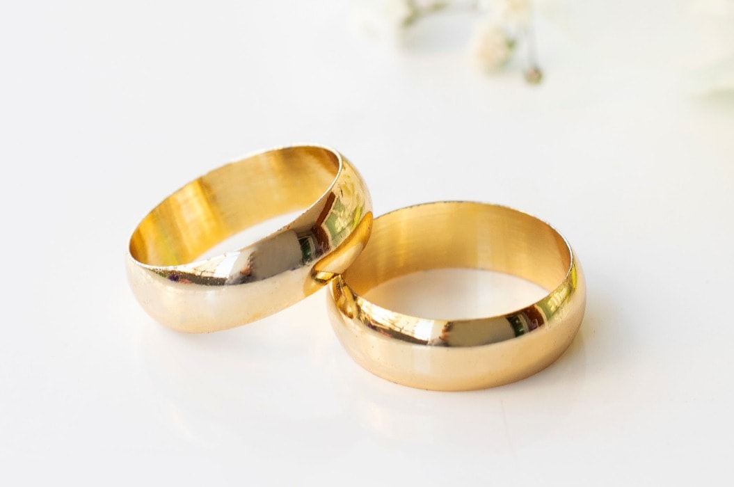 White flowers and two golden wedding rings on white background.